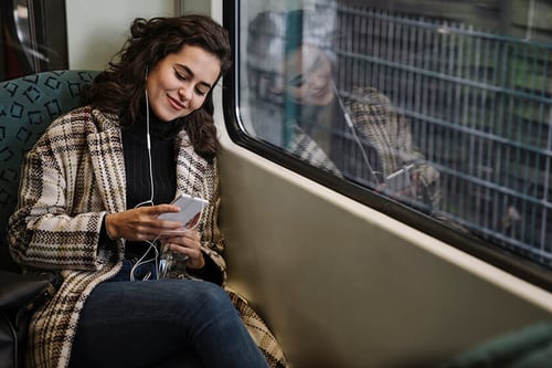 woman on train looking at phone and listening to music