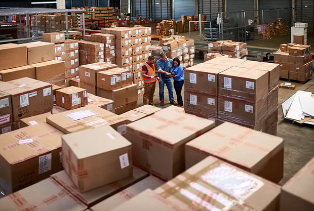 three people talking in middle of warehouse filled with boxes three people talking in middle of warehouse filled with boxes