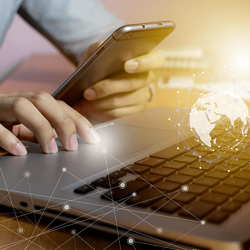 Global Scale Image of individual using a laptop and mobile device with overlay graphic of the globe