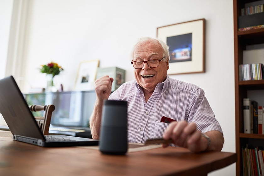  Hombre mayor comprando online con una tarjeta de crédito, un portátil y un dispositivo de altavoz inteligente.